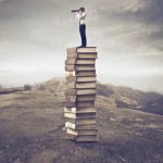 14022415 - young businessman standing on a stack of books and using a telescope